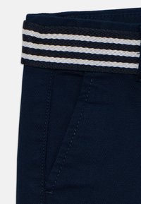 Pantalon bleu marine avec poche avant inclinée et ceinture élastique noire comportant deux bandes horizontales blanches.