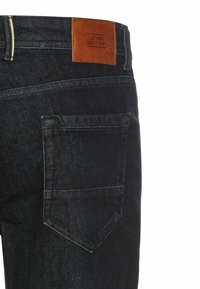 Donkerdenim jeans met een bruine leren patch met het "camel active" logo, zichtbare achterzak en contrasterende stiksels.