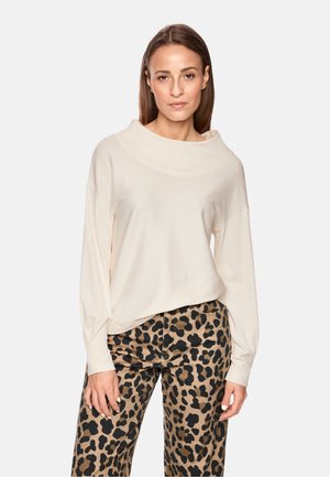Cremefarbener langärmeliger Oberteil mit Rundhalsausschnitt. Kombiniert mit Hose im Leopardenmuster in neutralen Tönen mit schwarzen Punkten. Einfaches Design.