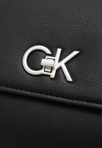 Black textured leather handbag featuring a silver metal logo clasp with interlocking letters "C" and "K." Sophisticated and modern design elements.