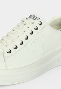 Baskets Guess basses blanches avec lacets blancs, œillets métalliques, logo embossé sur le côté et logo imprimé sur la languette.