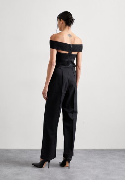 Top negru off-shoulder din material texturat, combinat cu pantaloni negri cu talie înaltă. Croi slim, detaliu cu fermoar la spate și tocuri înalte.