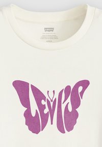 Bílý bavlněný tričko s velkým grafickým motivem fialového motýla, do kterého je integrován nápis "Levi's". Kulatý výstřih, krátké rukávy.