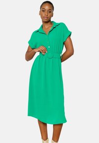 Vestito camicia verde con colletto, maniche corte, chiusura a bottoni davanti e cintura in tessuto abbinata. Le pieghe aggiungono un tocco di eleganza al design.
