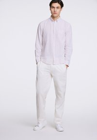 Camisa de manga larga, abotonada, en rosa claro con finas rayas y un bolsillo en el pecho, combinada con pantalones blancos de corte suelto y zapatillas blancas.