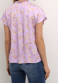 Krátký rukáv fialová blůza s květinovým vzorem v žluté a růžové barvě. Má volánkový výstřih a uvolněný střih.