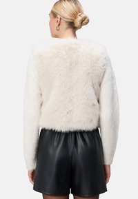 Cremfarbener Kunstpelzmantel mit weicher Textur, langen Ärmeln und cropped Design. Kombiniert mit schwarzen Leder-Shorts, die einen eleganten Look verleihen.