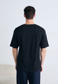 Camiseta de algodón negra con un corte relajado, mangas cortas y cuello redondo. Textura suave y diseño minimalista, vista desde la parte trasera.