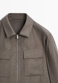 Giacca in misto lana marrone con zip frontale, colletto a punta e due tasche sul petto. Il tessuto presenta un aspetto texturizzato con dettagli sottili.