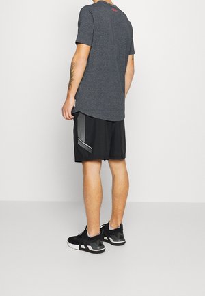Tenue de sport pour homme comprenant un t-shirt à manches courtes gris foncé et un short noir avec un motif réfléchissant diagonal. Des baskets noires complètent la tenue.