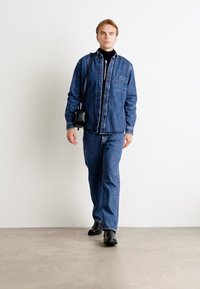Chaqueta de denim y jeans en azul oscuro, combinados con un cuello de tortuga negro. Textura suave, diseño de botones y un bolsillo en el pecho de la chaqueta.