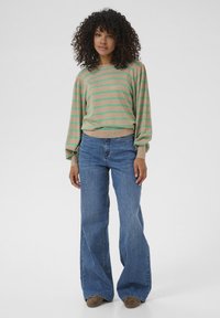 Maglione beige con righe verdi, maniche a palloncino e orlo a costine, abbinato a jeans a vita alta blu svasati e scarpe marroni.