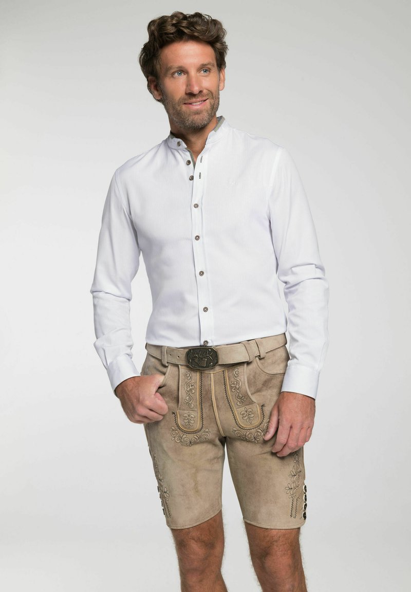 Weißes Langarmhemd mit Knopfleiste, kombiniert mit braunen Wildledershorts mit bestickten Blumenmustern und einer dekorativen Gürtelschnalle.