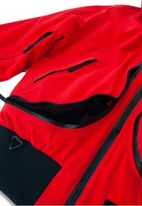 Piros cipzáras kabát fekete részletekkel, texturált anyaggal, zsebekkel és rugalmas mandzsettákkal. A cipzárnál sima bélés látható.