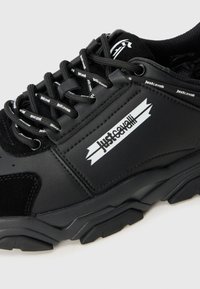 Svart Just Cavalli sneaker med merkede lisser og side-logo, med teksturert såle og blandede lær- og meshmaterialer.