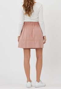 Jupe mini en daim rose avec une taille élastique et un design à volants. Portée avec des baskets blanches et un haut blanc à manches longues.