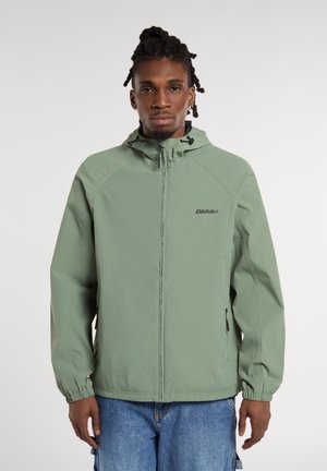 Chaquetón ligero de color verde claro con capucha. Cuenta con puños elásticos y bolsillos laterales con cremallera. Logotipo de la marca en el pecho.