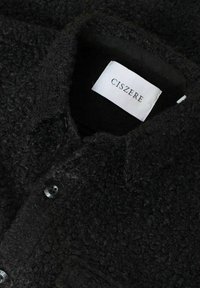Sort fleece skjorte med en tekstureret stof, med en knapkrave og en label, der tydeligt viser "CISZERE" indeni.