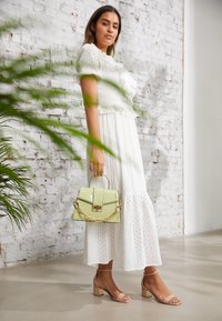 White, eyelet dress with ruffled details, complemented by a light green textured handbag with a gold chain. Beige strappy block heels.