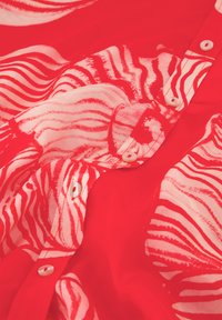 Rote Bluse mit einem Zebra-Streifen-Muster in Pink. Verfügt über Knopfverschlüsse und eine glatte, leichte Textur, die das mutige Design unterstreicht.
