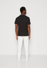 Sort kortærmet T-shirt med en simpel rund halsudskæring, fremstillet af blødt bomuldsstof. Bæres med hvide bukser og sneakers.