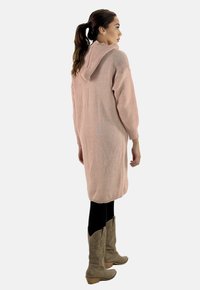 Strickkleid mit Kapuze in sanftem Rosa, mit gerippter Textur, Dreiviertelärmeln und lockerer Passform, kombiniert mit hellbraunen Cowboy Stiefeln.
