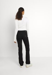 Jeans negros con un diseño ajustado y un leve acampanado, combinados con una parte superior blanca de canalé. La vista posterior muestra un estilo minimalista y un detallado sutil.