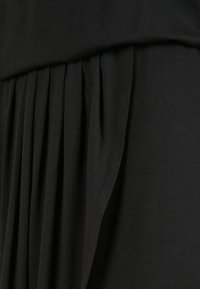 Lähikuva mustast kangaast, millel on vasakul vertikaalsed voltid ja paremal sujuv tekstuur, kus on näha õmblusest üksikasju.