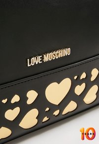 Černá kožená kabelka s výřezovými srdíčky a zlatým podkladem. Značková "LOVE MOSCHINO" ve stříbrném metalickém písmu.