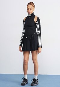 Black long-sleeve top with open shoulders, white stripes, and logo; matching black drawstring skirt; black sneakers and white socks.