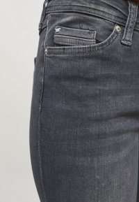 Los vaqueros de mezclilla oscura cuentan con un ajuste slim, un bolsillo delantero con un pequeño detalle rasgado y acentos de metal plateado. Textura suave y color profundo.