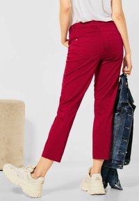 Red cropped pants made of stretchy fabric, featuring back pockets and a fitted waist, paired with beige sneakers and a denim jacket.