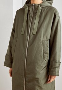 Olive green, ocieplana kurtka parka z kapturem. Posiada pełny zamek z przodu, dwie boczne kieszenie oraz regulowany sznurek w kapturze.