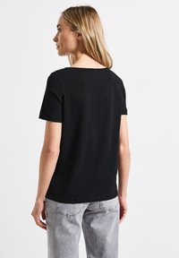 T-shirt noire à manches courtes avec un col rond, fabriquée en tissu lisse. Associée à un pantalon gris clair, avec une coupe décontractée.