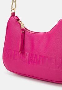 Sac à main synthétique rose avec une finition texturée, doté d'une fermeture éclair et d'un détail de logo en relief. Des accents en métal doré rehaussent le design.