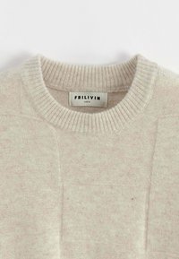 Pull beige clair avec un col rond, tricot texturé et un motif discret. L'étiquette indique "FRILIVIN TAILLE M". Finition du tissu lisse.
