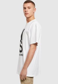 Hvid bomulds t-shirt med korte ærmer, prydet med et stort sort grafisk print på forsiden. Casual, afslappet pasform.