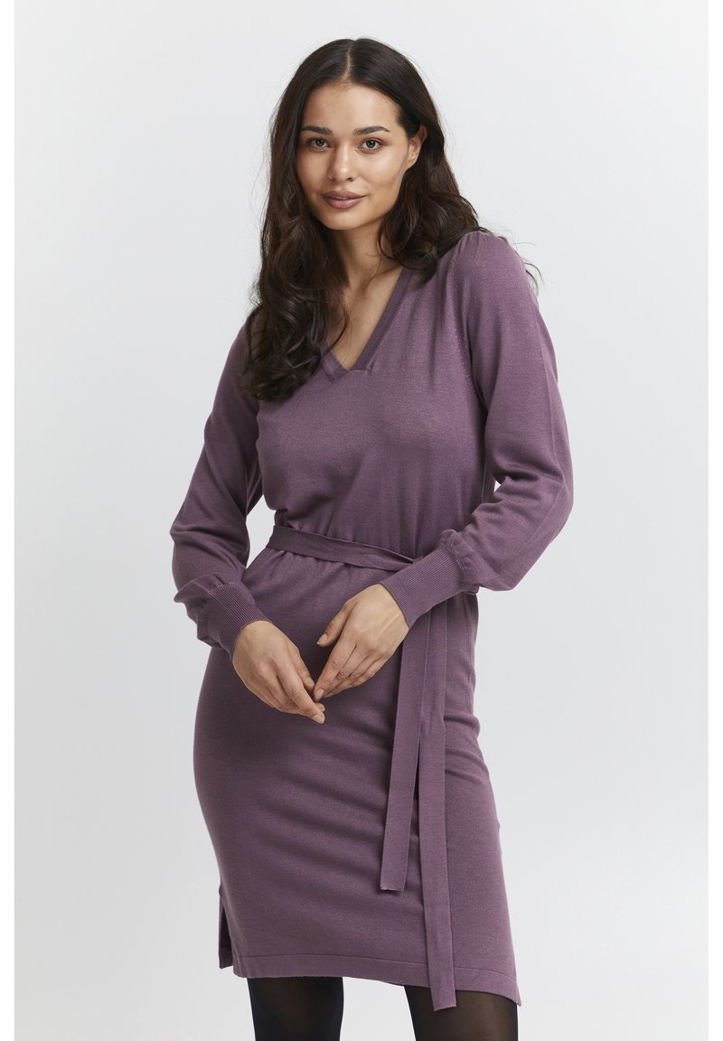 Abito a maniche lunghe con scollo a V in morbido maglione viola; presenta una cintura annodata in vita e spacchi laterali per facilitare i movimenti.
