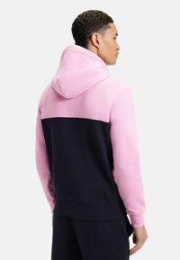 Sweat-shirt à capuche avec une partie supérieure rose et une partie inférieure navy, fabriqué en tissu doux. Il dispose d'une poche kangourou et de poignets côtelés.