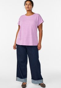 Rosa T-Shirt mit kurzen Ärmeln und rundem Ausschnitt, kombiniert mit weiten, dunkelblauen Jeans mit umgeschlagenem Saum. Braune Schuhe runden den Look ab.
