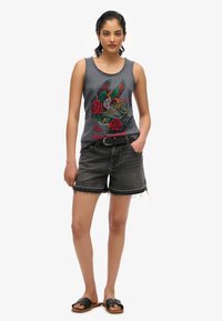 Grijze grafische tanktop met een adelaar en rozen, gecombineerd met zwarte denim shorts met een rafelige zoom, gedragen met zwarte slippers.