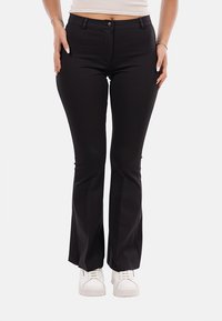 Pantaloni neri a campana realizzati in tessuto elasticizzato, con chiusura frontale a bottone e tasche. Abbinati a sneakers bianche.