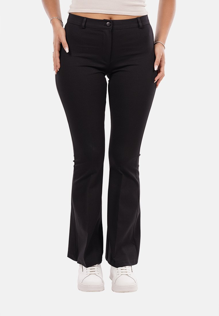 Pantaloni neri a campana realizzati in tessuto elasticizzato, con chiusura frontale a bottone e tasche. Abbinati a sneakers bianche.
