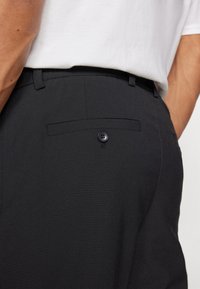 Svarta tygbyxor med en slät yta, som har en bakficka och en stängning med två knappar. Midjan sitter tajt och designen är skräddarsydd.