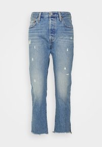 Jeans de mezclilla azul claro con corte recto, detalles desgastados y dobladillo con flecos. Cuenta con cinco bolsillos y un cierre de botón tradicional.