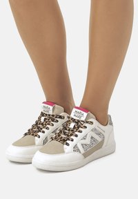 Zapatillas blancas con cordones de print de leopardo y acentos grises, con un panel lateral brillante y una etiqueta de logo en rosa en el talón. Materiales texturizados.
