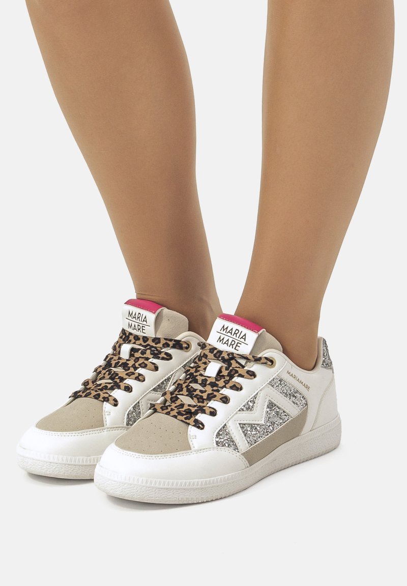 Zapatillas blancas con cordones de print de leopardo y acentos grises, con un panel lateral brillante y una etiqueta de logo en rosa en el talón. Materiales texturizados.