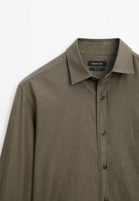 Chemise olive verte à manches longues avec boutons sur le devant et col classique, dotée de l'étiquette Massimo Dutti à l'intérieur du col.