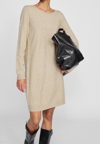 Abito in maglia beige con maniche lunghe, polsini a costine e orlo. Abbinato a una borsa a tracolla in pelle nera e stivali neri al ginocchio.