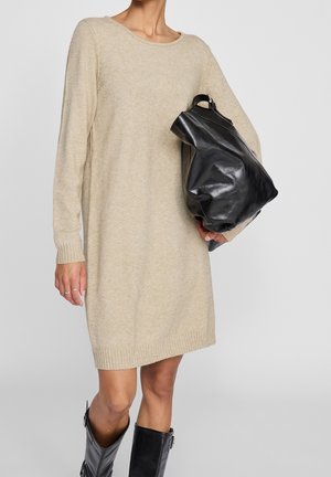 Abito in maglia beige con maniche lunghe, polsini a costine e orlo. Abbinato a una borsa a tracolla in pelle nera e stivali neri al ginocchio.